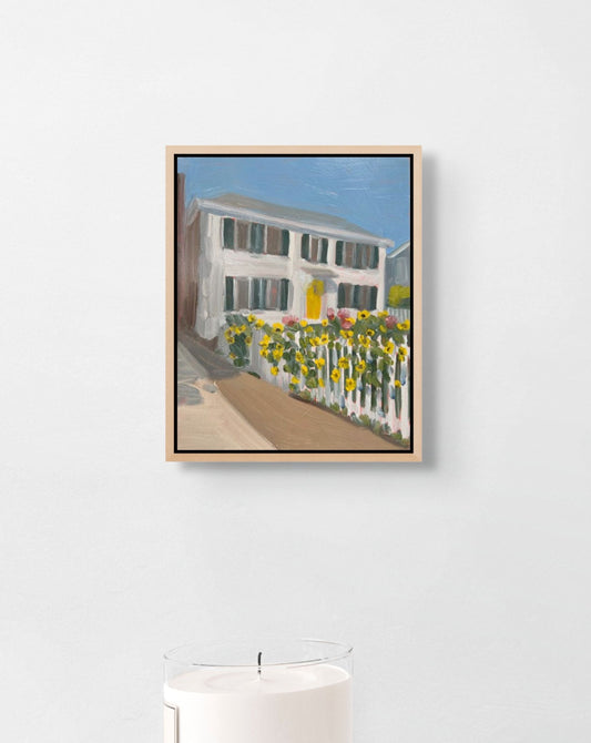 Framed painting of a house with flowers on a white wall