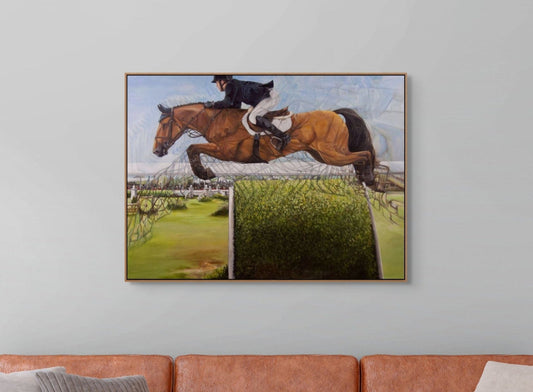 Framed painting of a horse and rider jumping over a fence on a wall above a sofa.