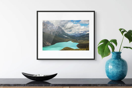 Framed landscape print of a mountain lake on a wall above a shelf with decorative items.