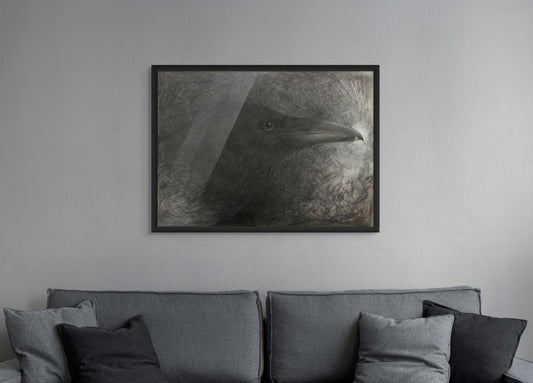 Framed artwork of a raven head on a wall above a gray sofa with cushions.