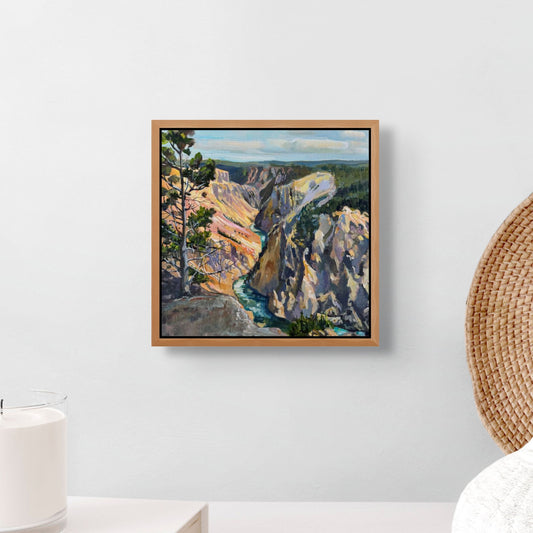 Framed painting of a canyon landscape on a wall with a candle and woven basket in the foreground.