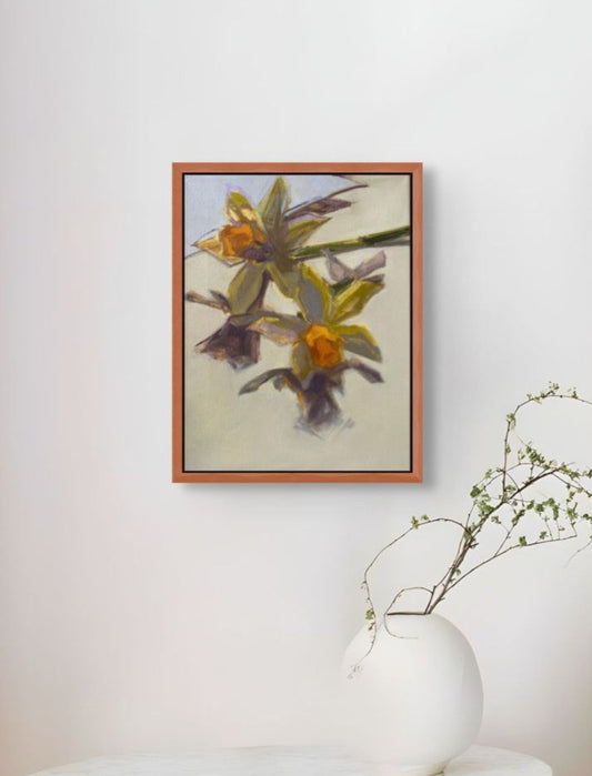 Framed artwork of flowers on a white wall with a vase and plant in the foreground.