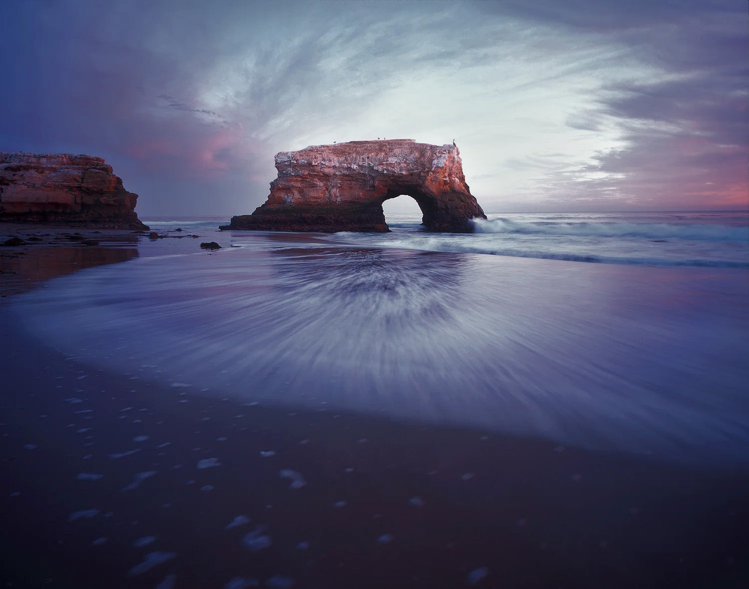 Rocks with a natural arch over a beach at sunset